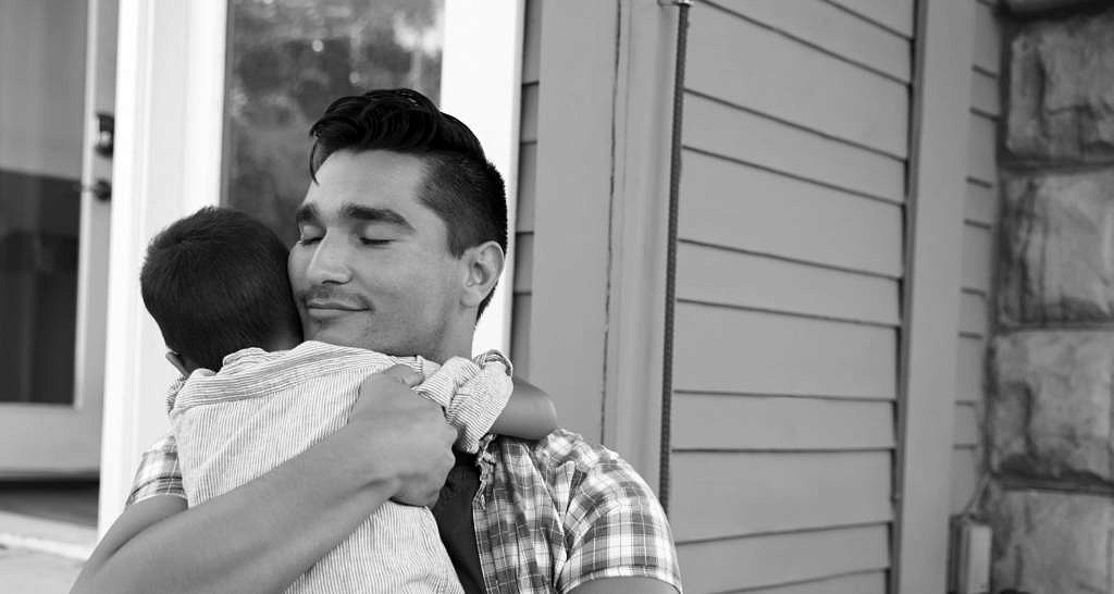 Father Hugging Son Sitting On Steps Outside Home