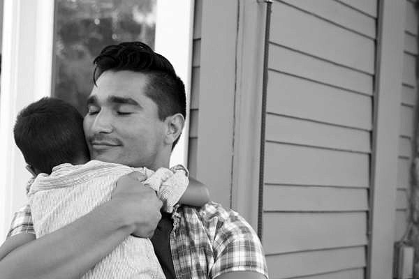 Father Hugging Son Sitting On Steps Outside Home