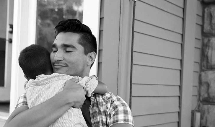 Father Hugging Son Sitting On Steps Outside Home