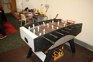 A foosball table against a wall near a table with a puzzle and some musical instruments 