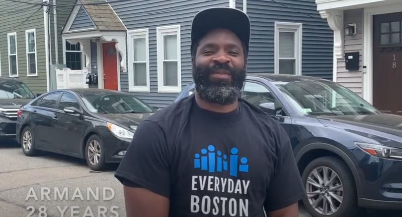 A man in a baseball cap stands on a city street