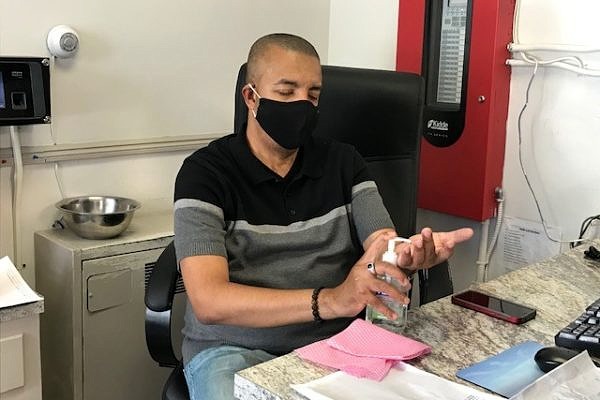 A man wearing a face mask uses hand sanitizer while sitting at a desk