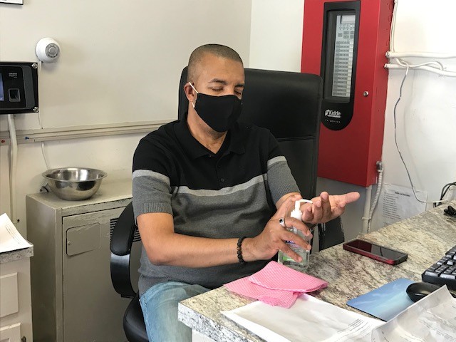 A man wearing a face mask uses hand sanitizer while sitting at a desk