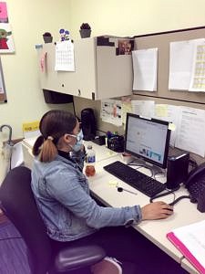 A woman wearing a face mask works at a computer. 