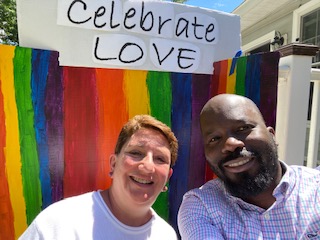 Two people smiling in front of a banner with rainbow colors and the words "Celebrate Love"