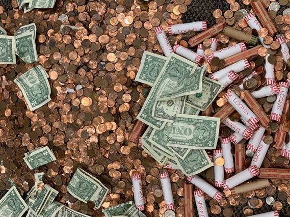 A heap of pennies, some loose and some in rolls, with dollar bills and other coins scattered throughout