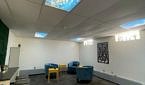 A spacious room with white walls, bright blue upholstered chairs, wooden tables, and sunlit windows