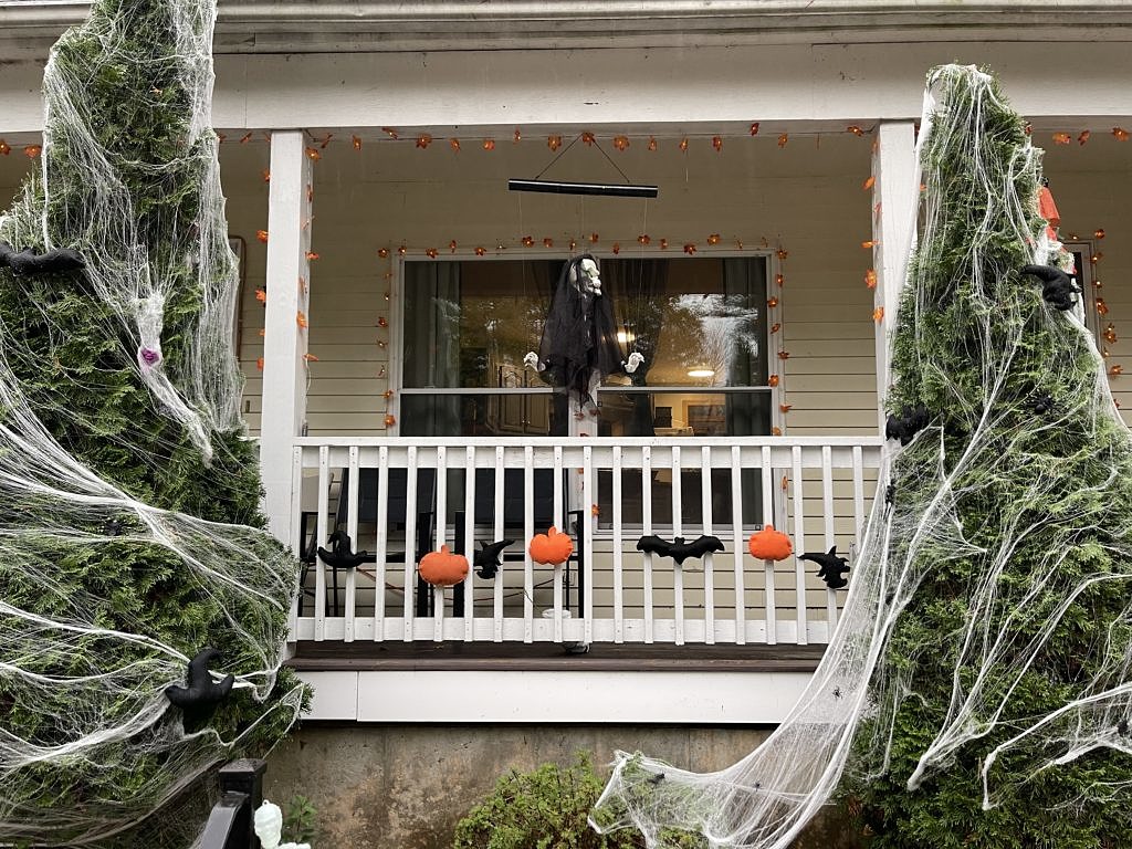 Halloween decorations on a front porch, including a skeleton with a veil, paper bats and pumpkins, and fake cobwebs