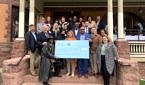 A group of people stand on the steps of a building smiling and holding a giant check