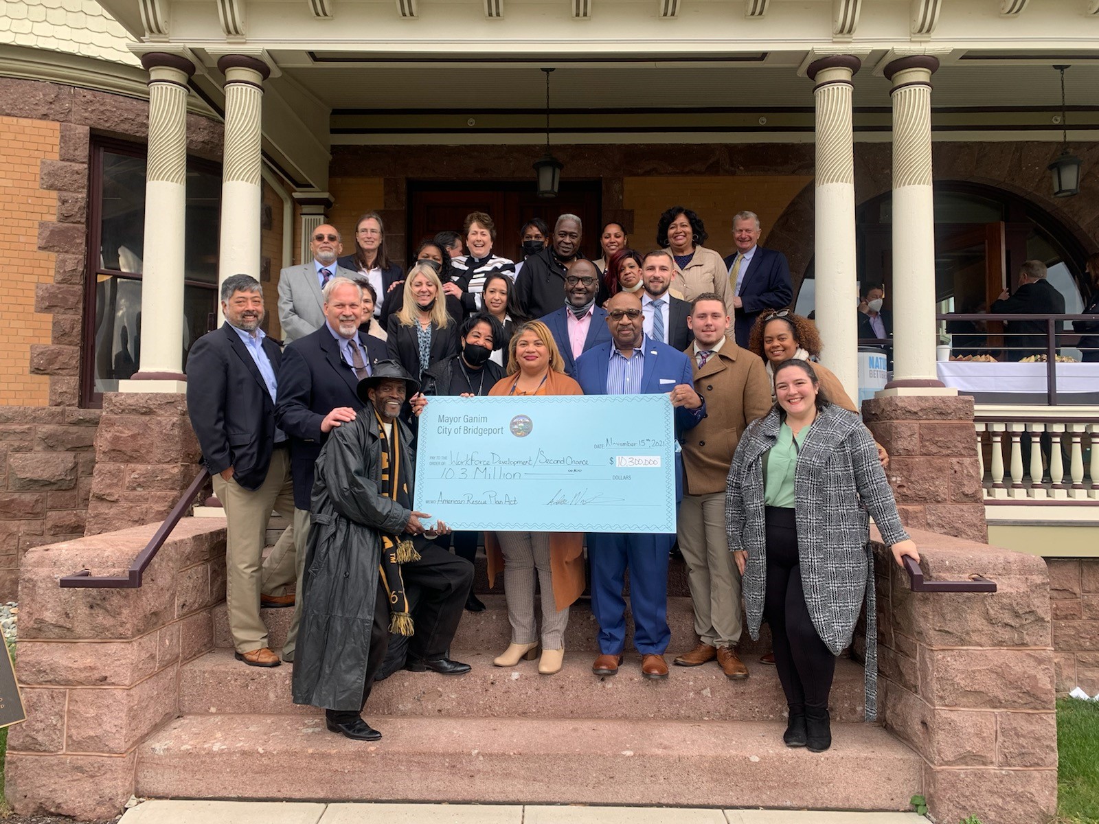 A group of people stand on the steps of a building smiling and holding a giant check