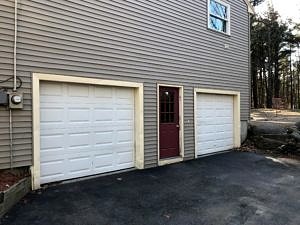 A photo showing the exterior before the renovation with a door in the center and large garage doors on either side